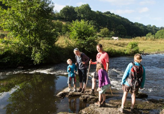 couple avec enfants en randonnée pédestre au bord d'une rivière bordée de champs