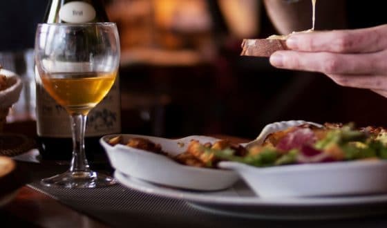 2 verres de cidre et un plat avec spécialité au fromage normand _ main d'une personne faisant une tartine de fromage normand